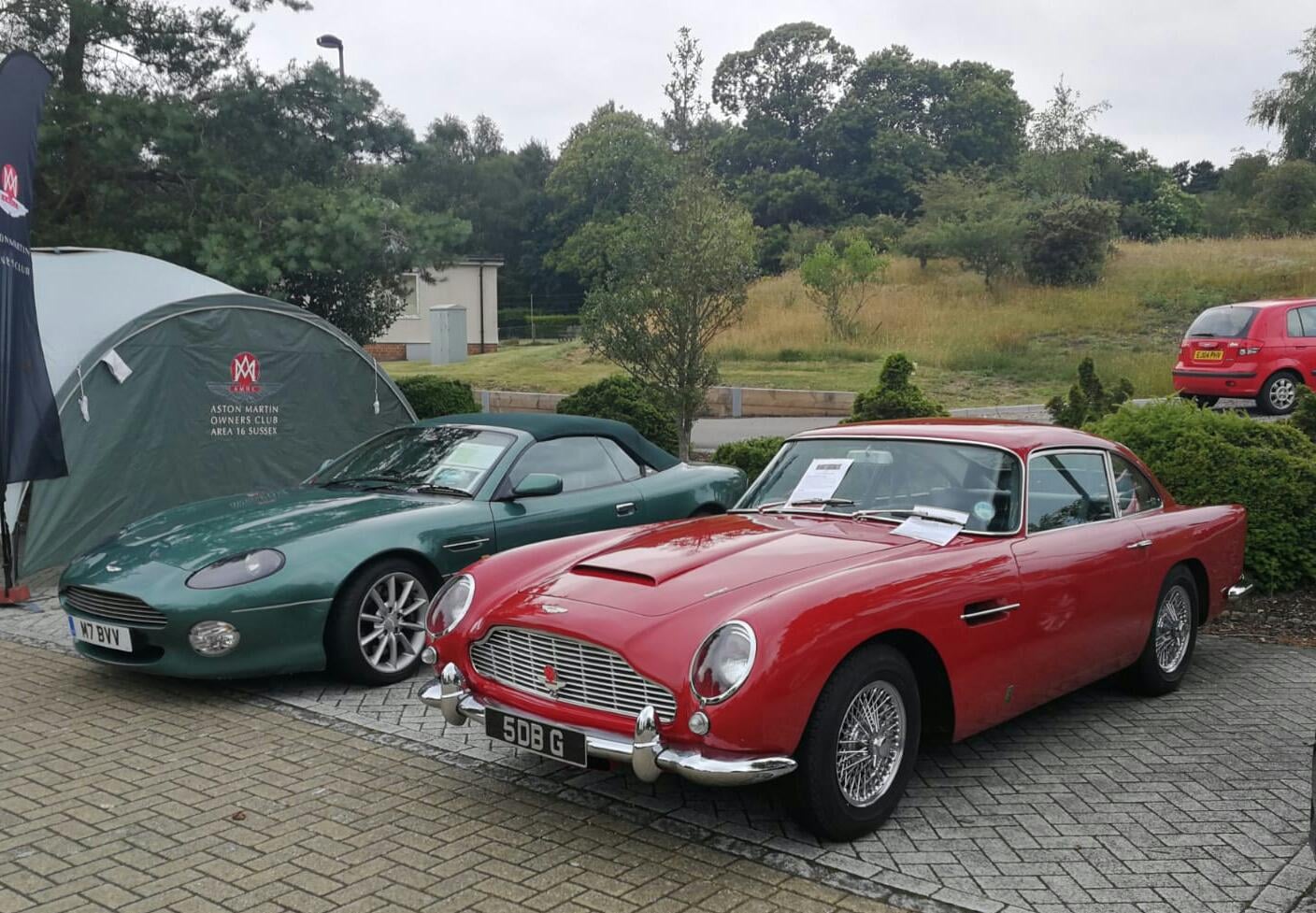 A green Aston Martin DB7 V12 Volante beside a red 1964 DB5