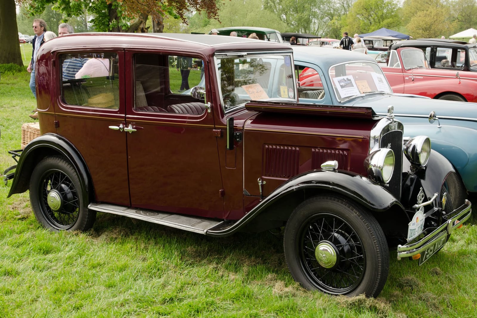 A maroon 1933 Austin Ten four-door saloon on grass at a vintage car rally, side view