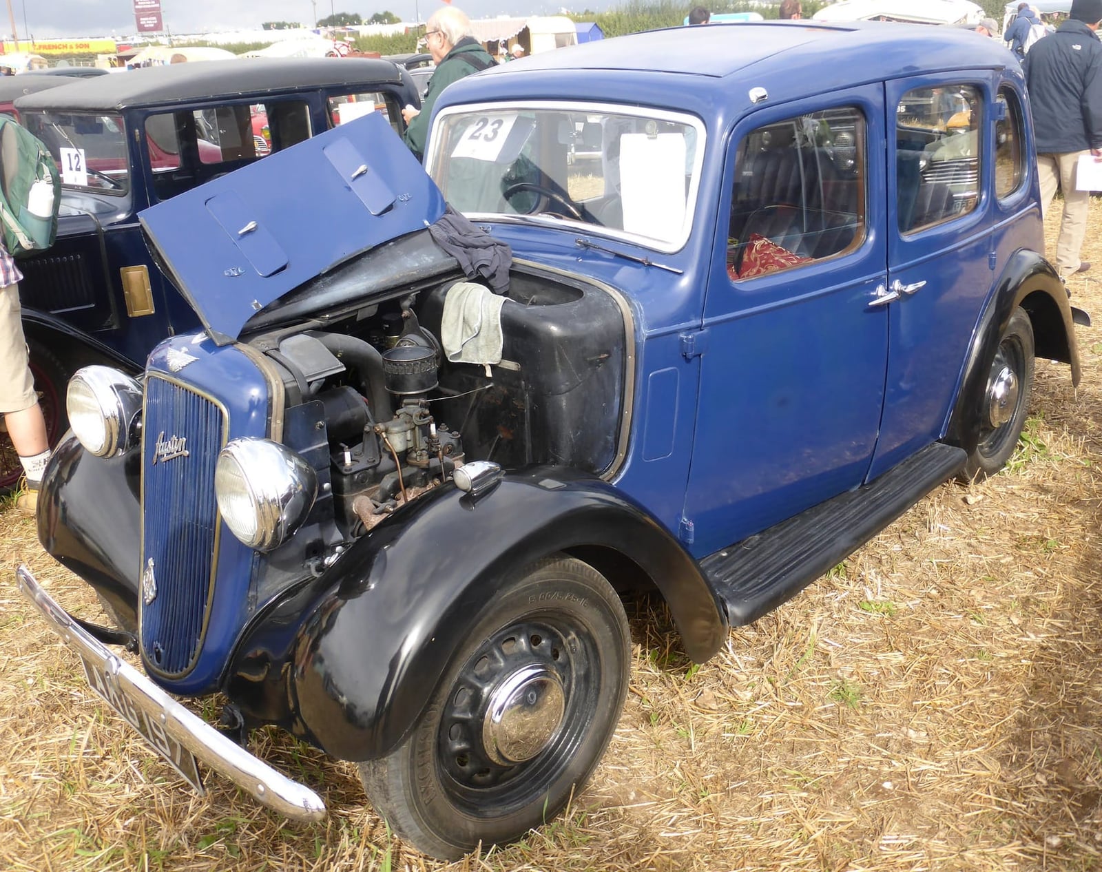 A blue 1937 Austin Ten Cambridge with its bonnet open on grass, engine visible