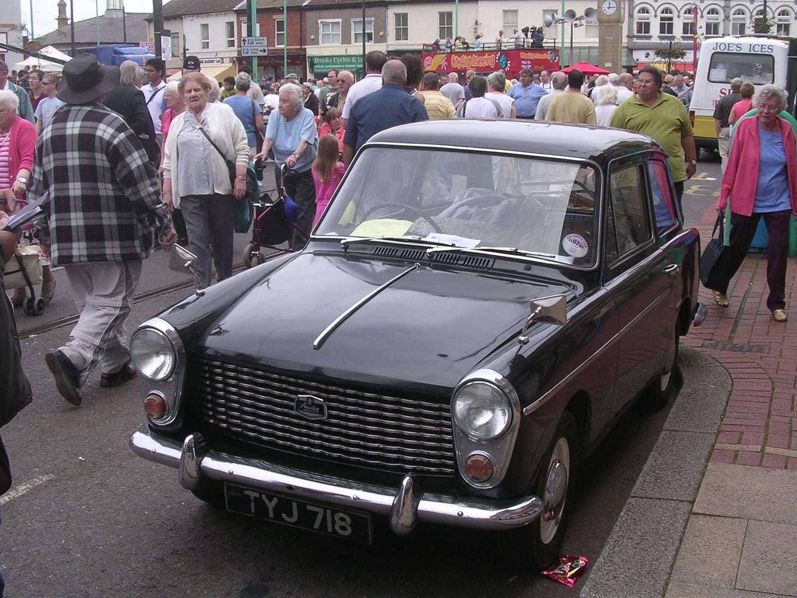 A black Austin A40 Farina parked on a town street during an event, front three-quarter view, UK registration TYJ 718