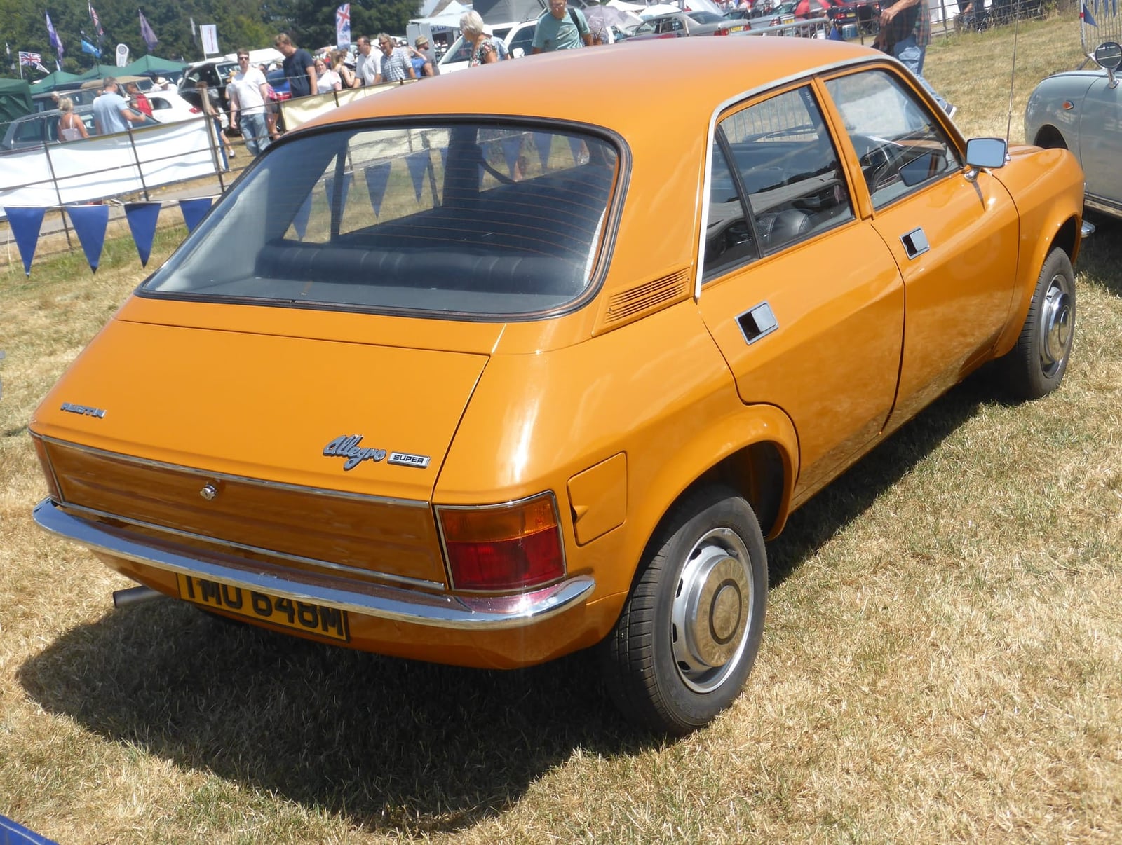 The rear three-quarter of an orange 1974 Austin Allegro 1300 Super on grass at a show