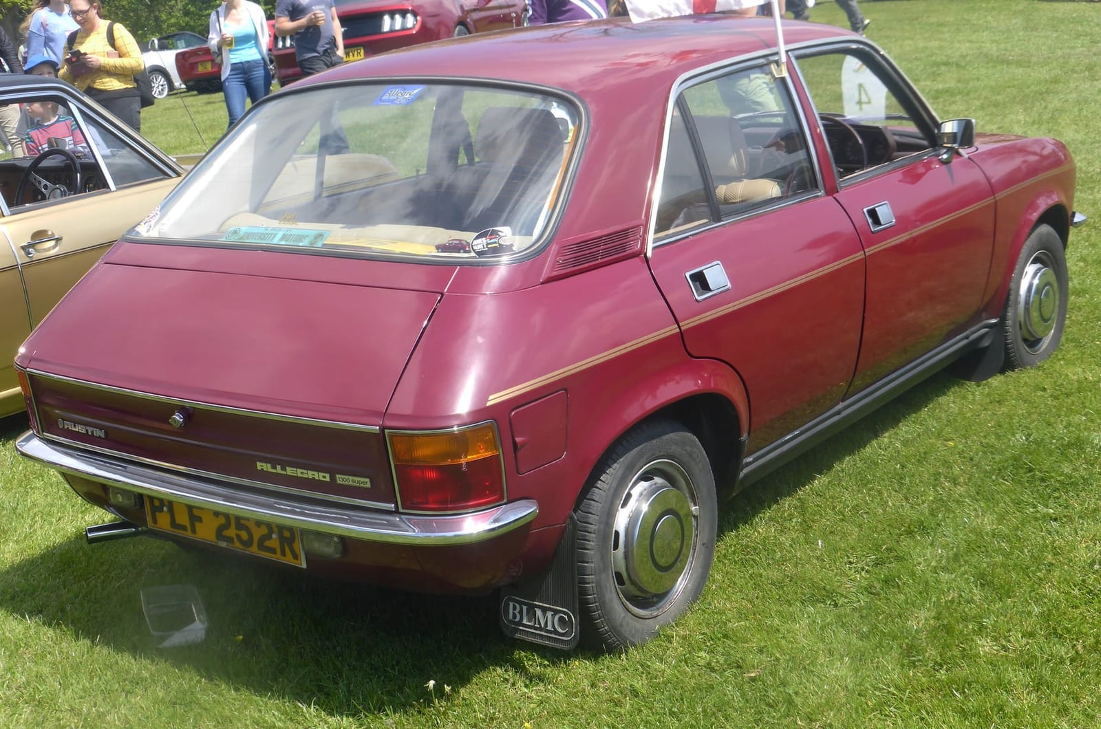 An orange Austin Allegro four-door on grass at a classic car show, front three-quarter view, UK registration YHU 649M