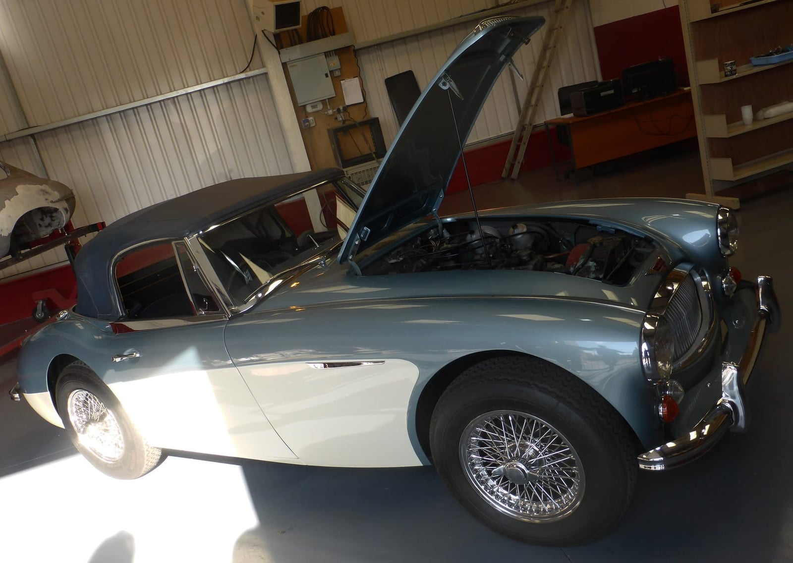 A two-tone Austin-Healey 3000 with its bonnet raised inside a home garage