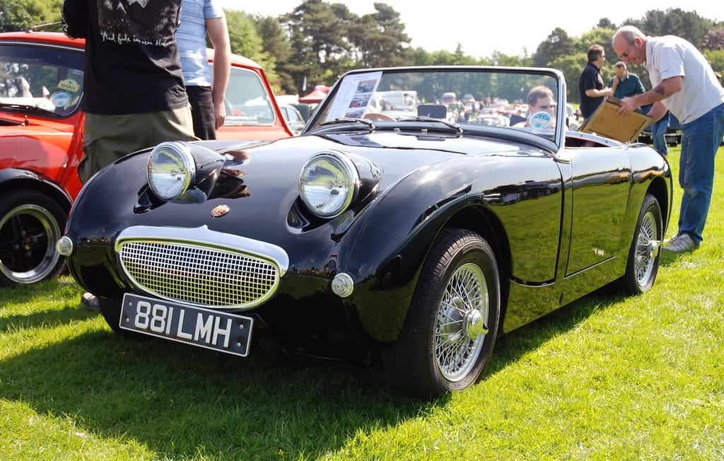 A black Austin-Healey Frogeye Sprite on wire wheels at a classic car show, front three-quarter view, UK registration 881 LMH