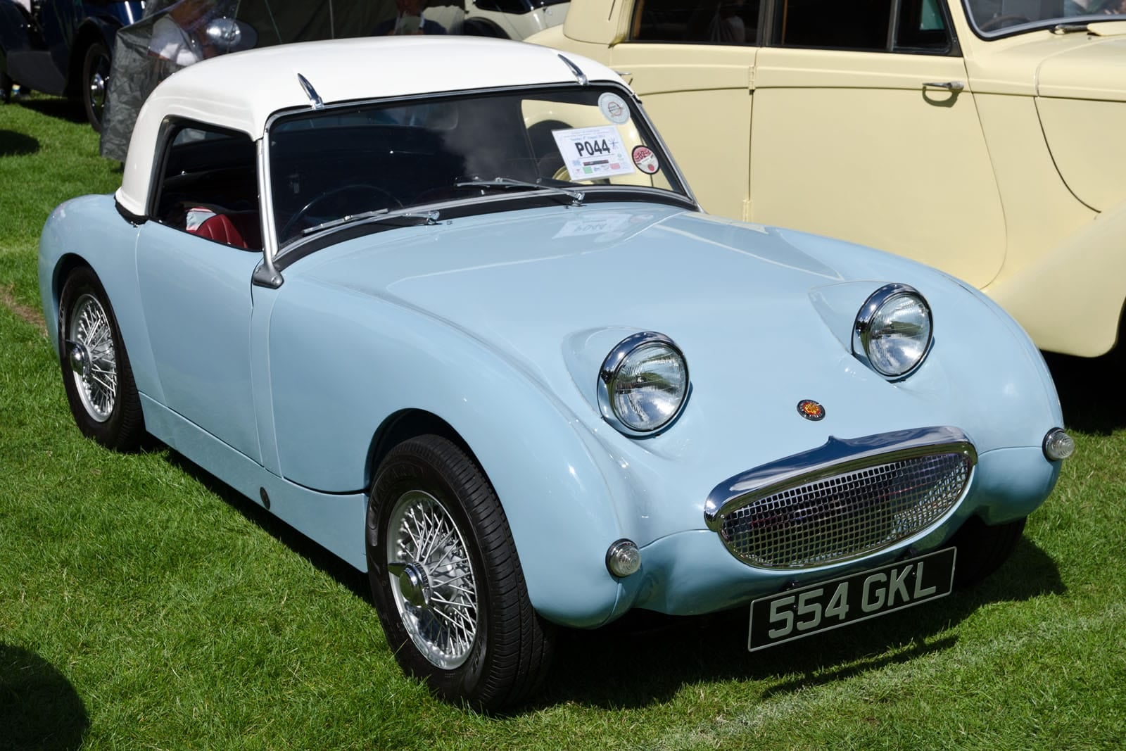 A pale blue 1959 Austin-Healey Sprite Mk1 with a hardtop fitted, on grass at a classic car show, front three-quarter view, UK registration 554 GKL