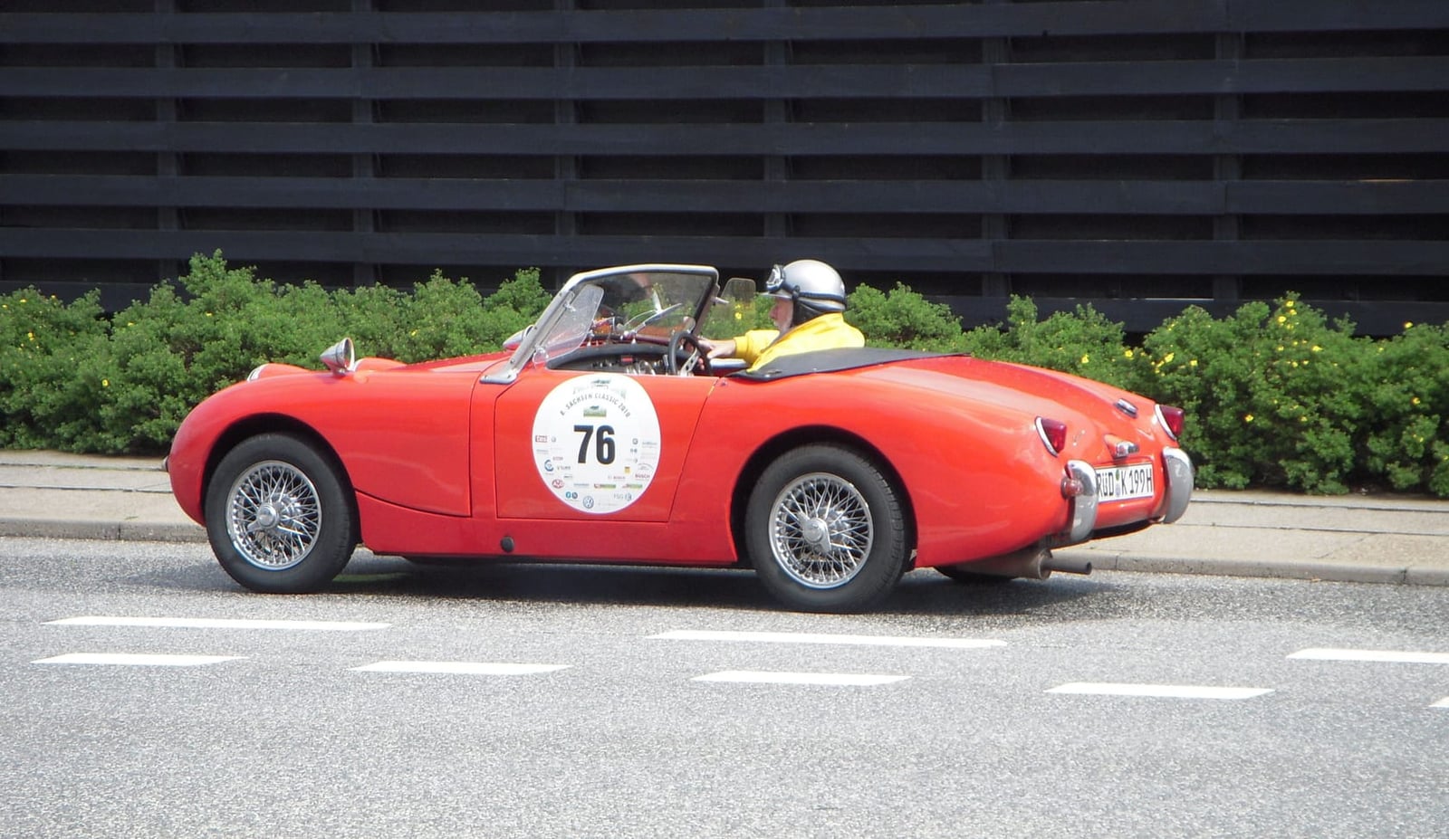 A red Austin-Healey Sprite Mk1 competition car carrying race number 76 on a road event, driver in helmet
