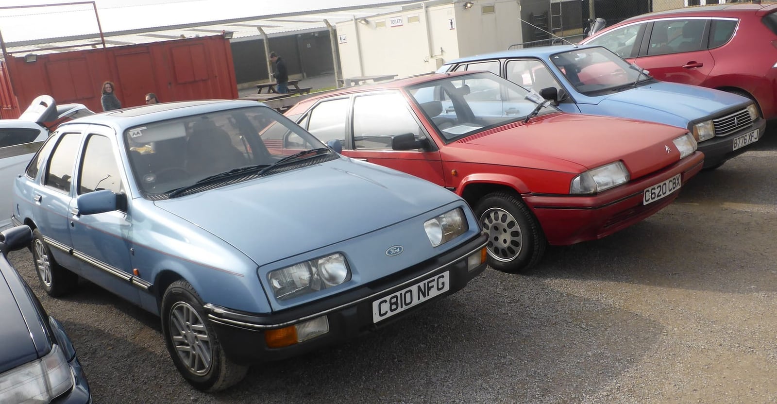 A light blue early Ford Sierra three-door among other 1980s cars at a classic gathering, UK registration C810 NFG