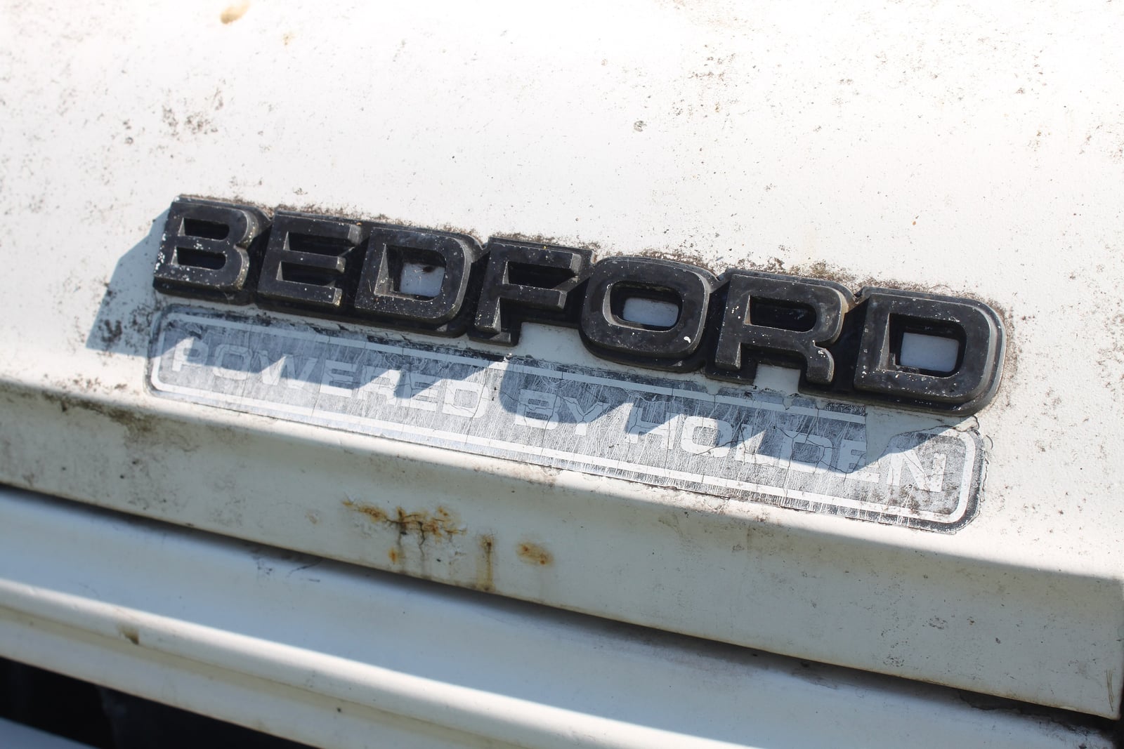 Close-up of the chrome BEDFORD badge above a faded "Powered by Holden" decal on the bodywork of a CF van