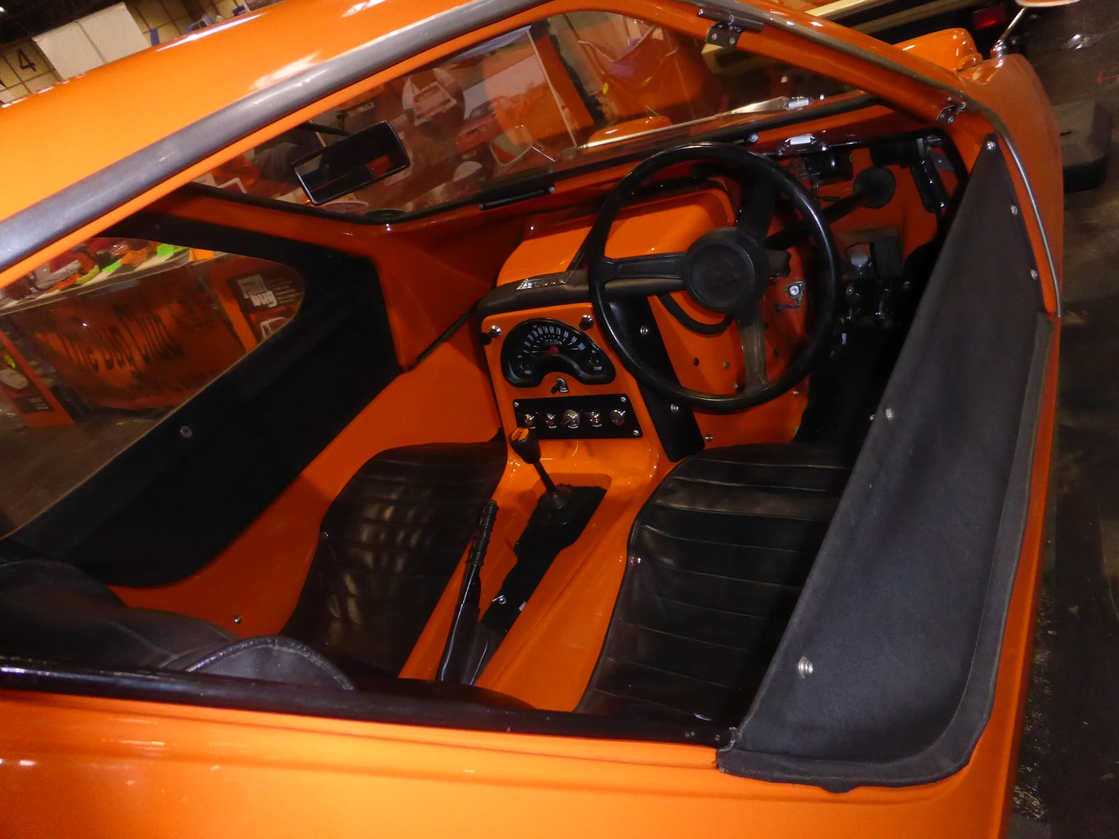 An orange 1971 Bond Bug three-wheeler on grass at a show, front three-quarter view showing the wedge nose and single front wheel