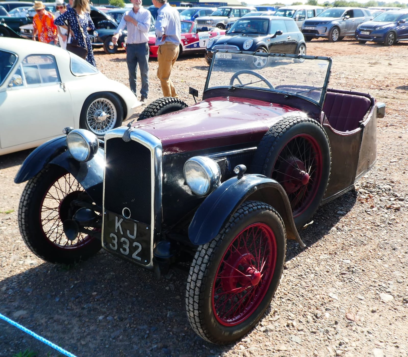 A maroon 1931 BSA three-wheeler on gravel at a classic vehicle show, front three-quarter view, UK registration KJ 332
