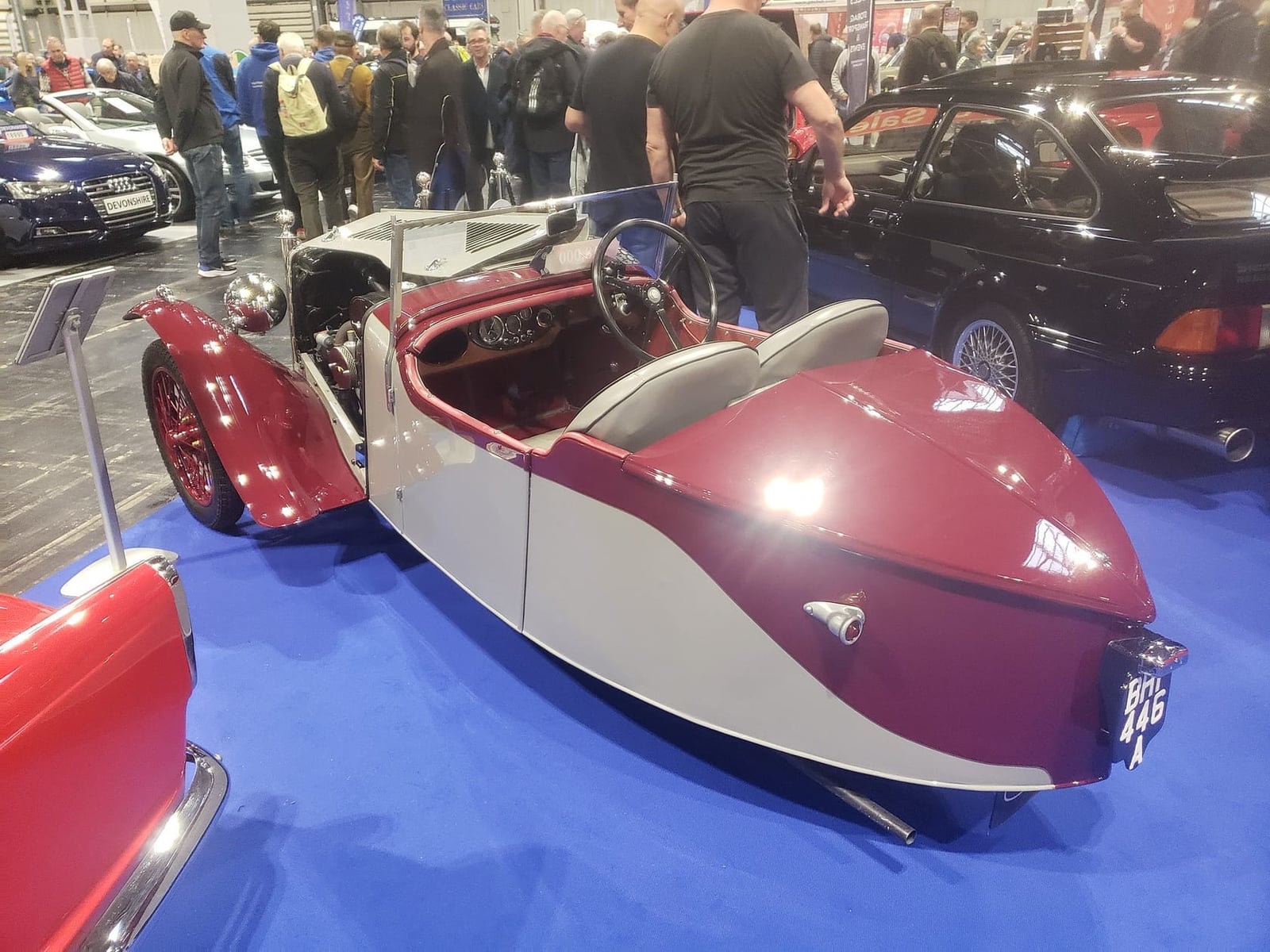 A maroon and cream 1934 BSA three-wheeler with streamlined bodywork on indoor display, rear three-quarter view