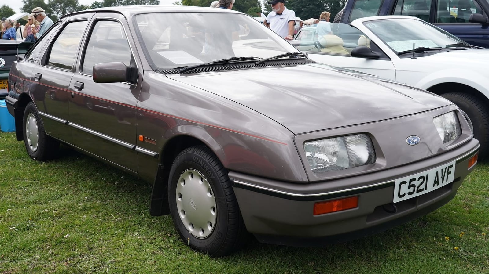 A grey Ford Sierra L five-door hatchback on grass at a classic car show, front three-quarter view, UK registration C521 AVF