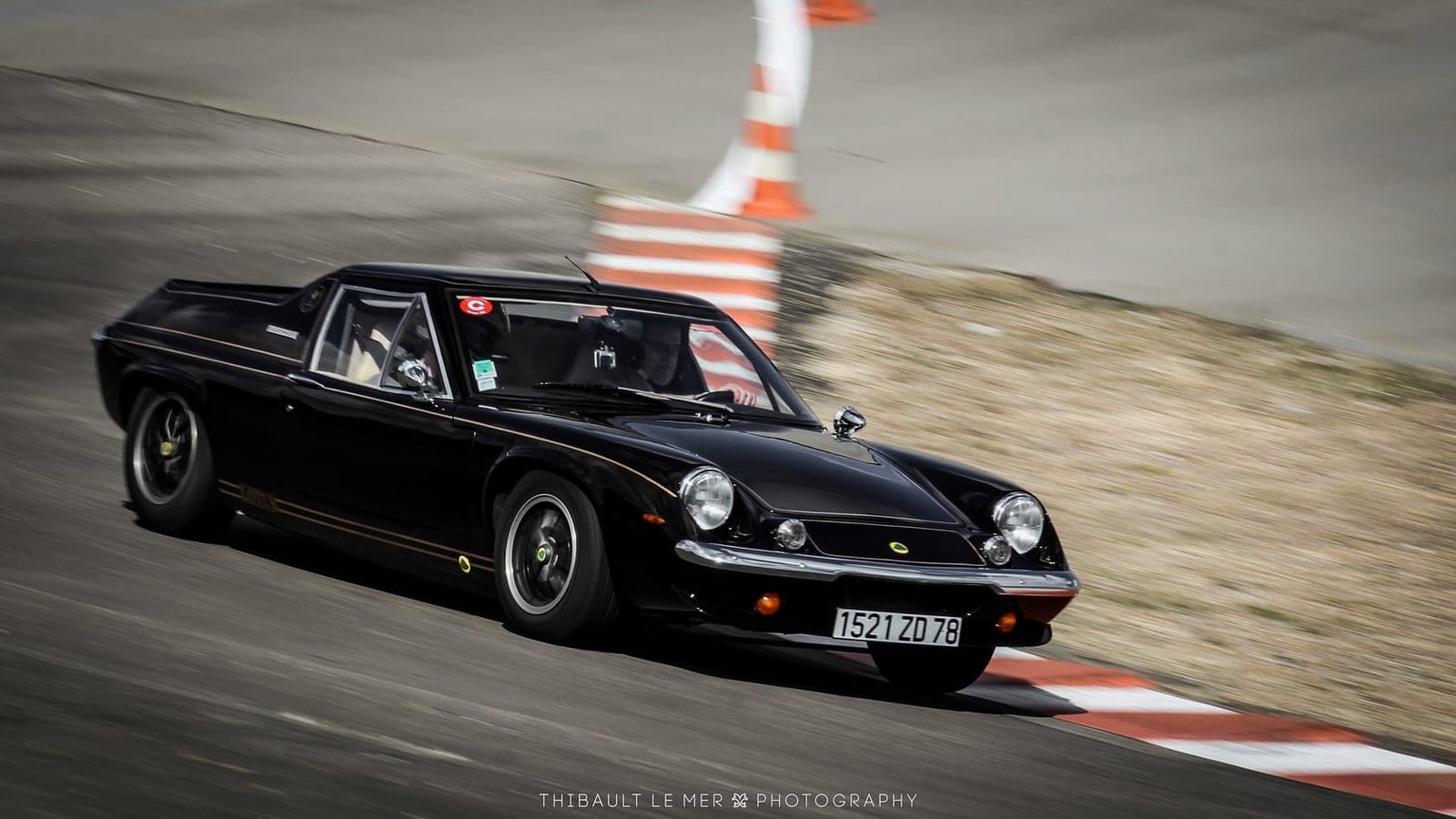 A black Lotus Europa cornering at speed on a race circuit with the apex kerb alongside