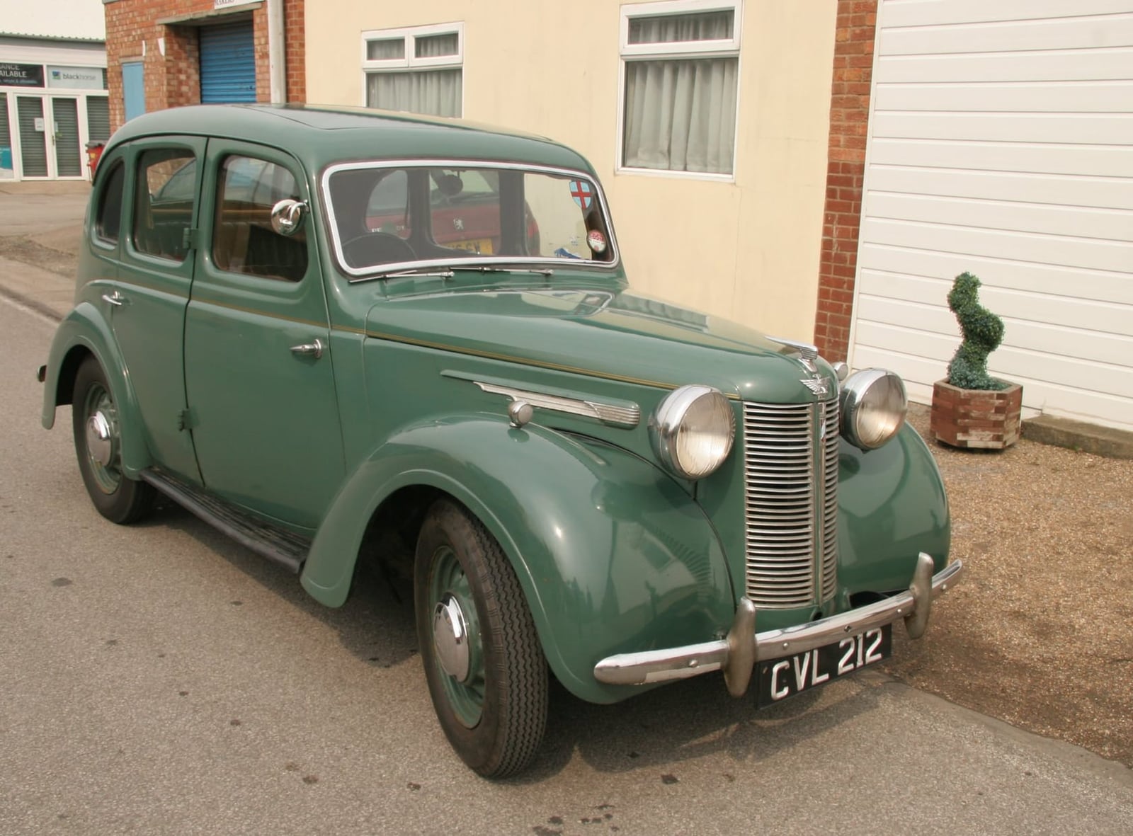 A green 1947 Austin Ten saloon parked beside a building, front three-quarter view, UK registration CVL 212