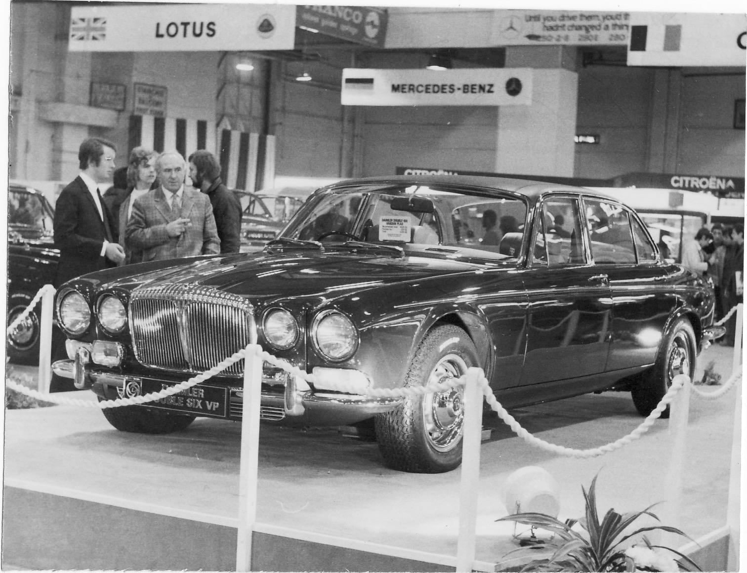 A period black and white photograph of a Daimler Double Six Vanden Plas on a roped-off motor show stand, with visitors looking on
