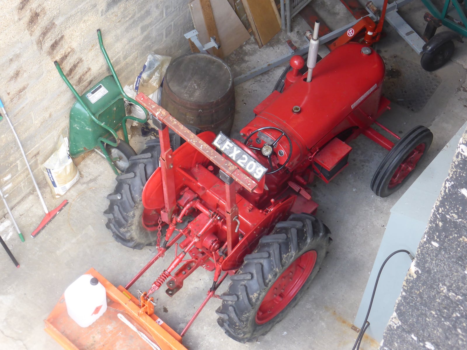 A red 1957 David Brown tractor with a mid-mounted toolbar implement, viewed from above in a yard