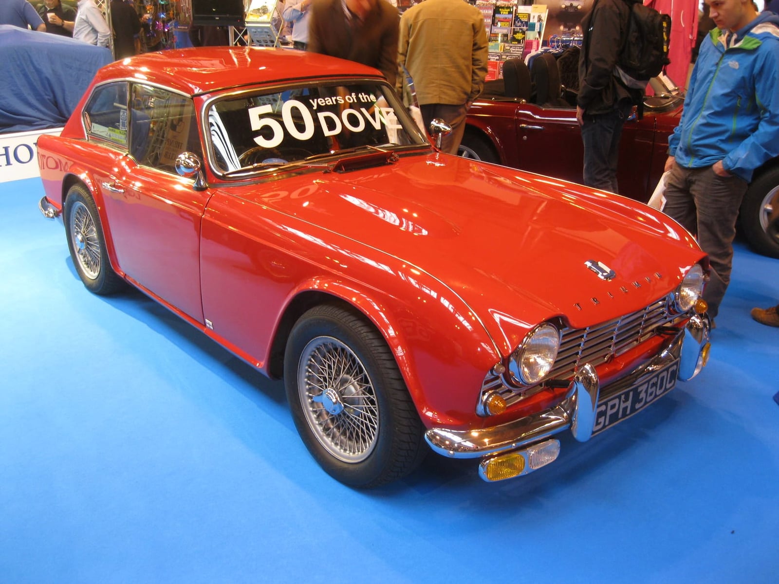A red Dove GTR4 fastback coupé based on the Triumph TR4, on a show stand with a fiftieth-anniversary sign