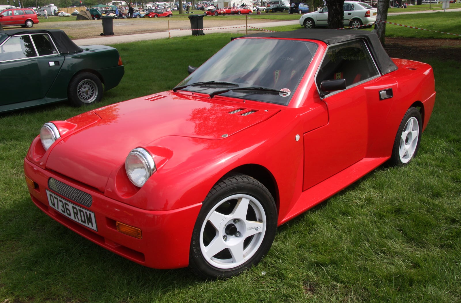 A red Dutton Legerra roadster with the soft top folded, front three-quarter view at a classic car show