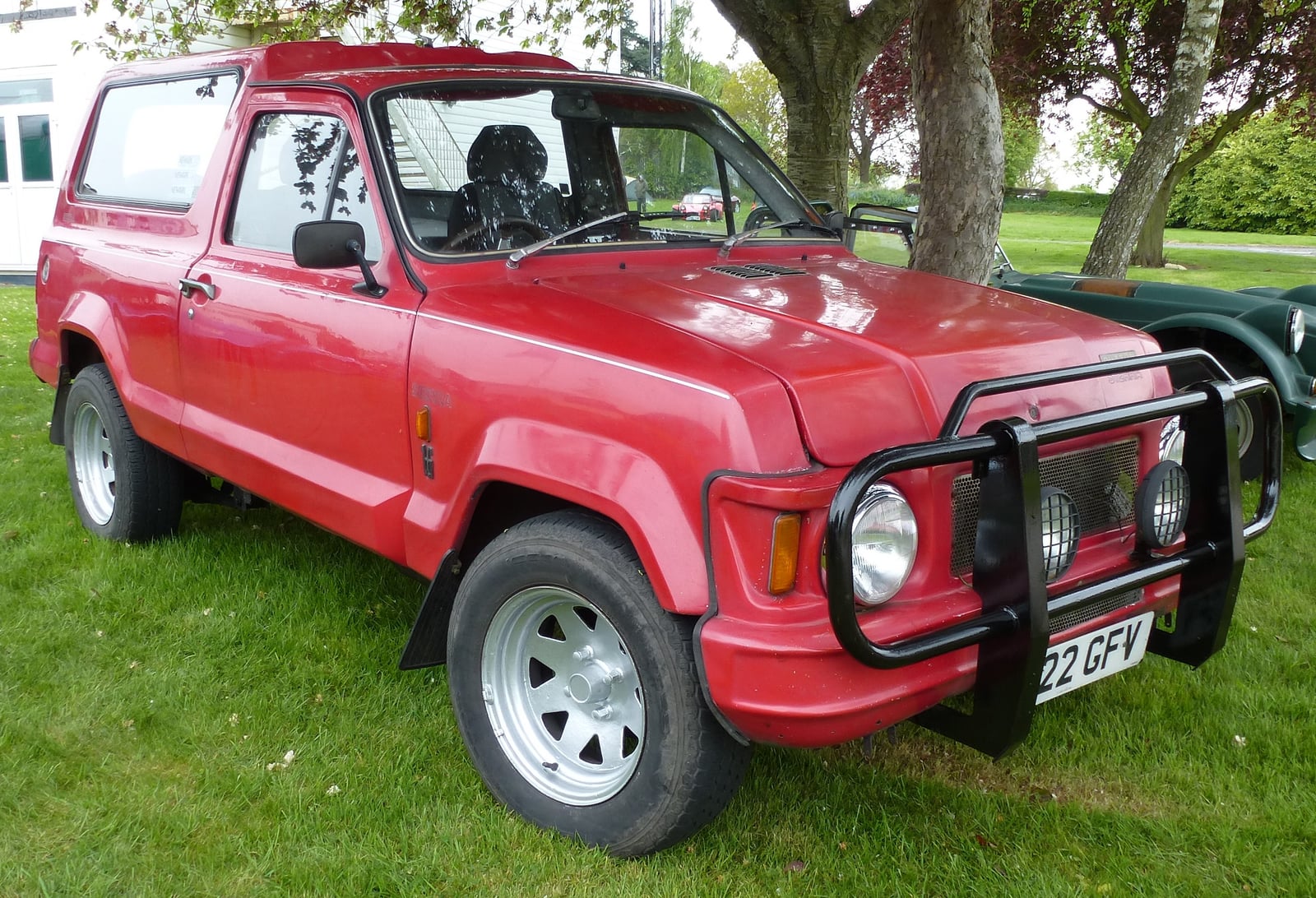 A red Dutton Sierra, a glass-fibre estate-style car with a rear-mounted spare wheel and chunky tyres, front three-quarter view at a classic car show