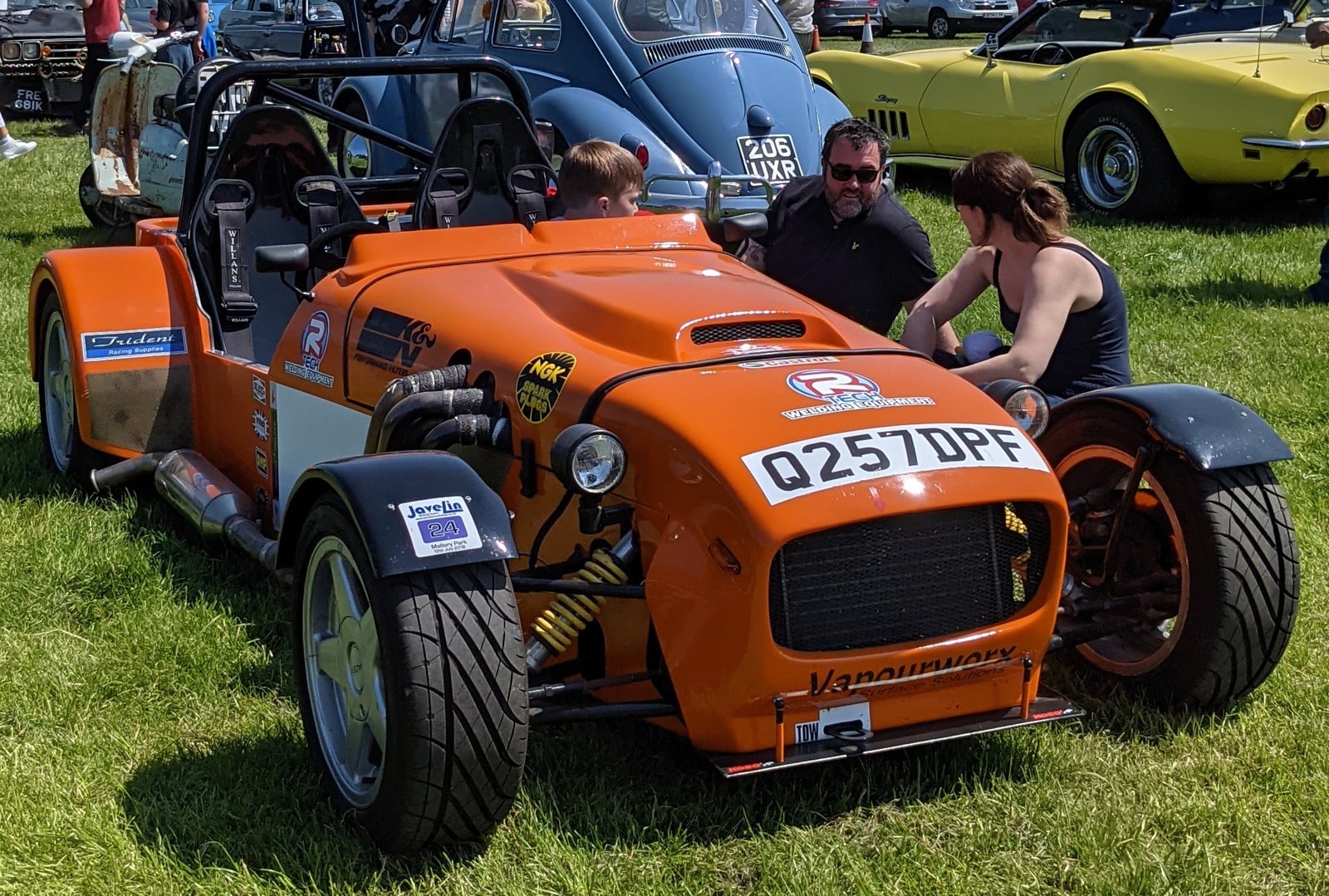 An orange Dutton Seven-style open roadster at a classic car show
