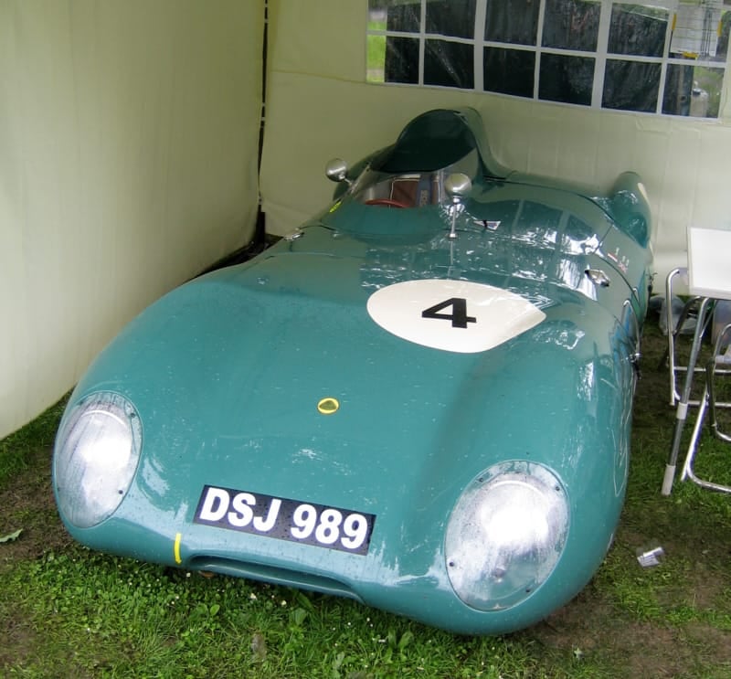 A green Lotus Eleven Series 1 carrying race number 4 parked beside a building, front three-quarter view, UK registration DSJ 989