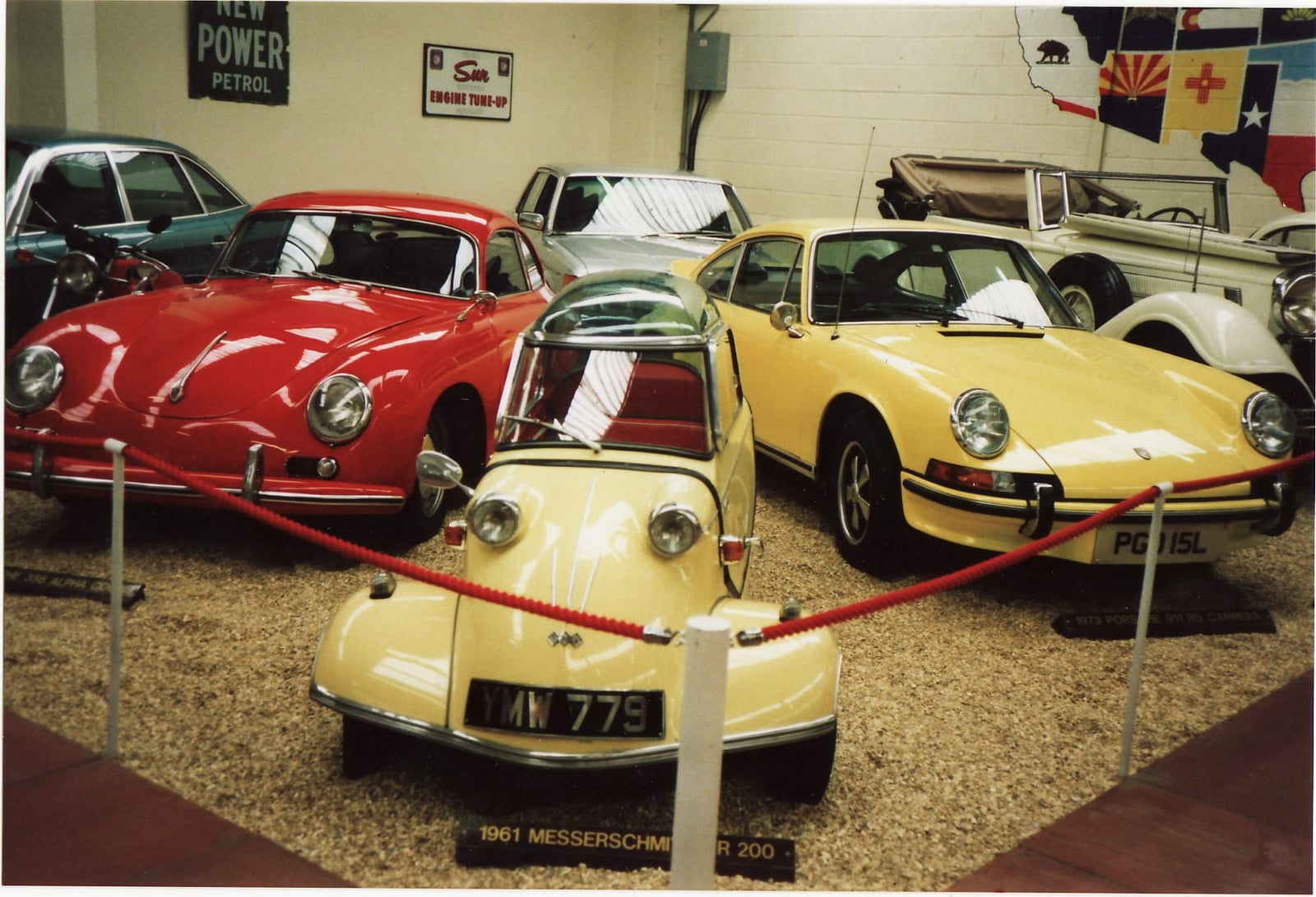 A yellow Messerschmitt 200 on museum display beside Porsche 356 and 911 models, UK registration MN 779