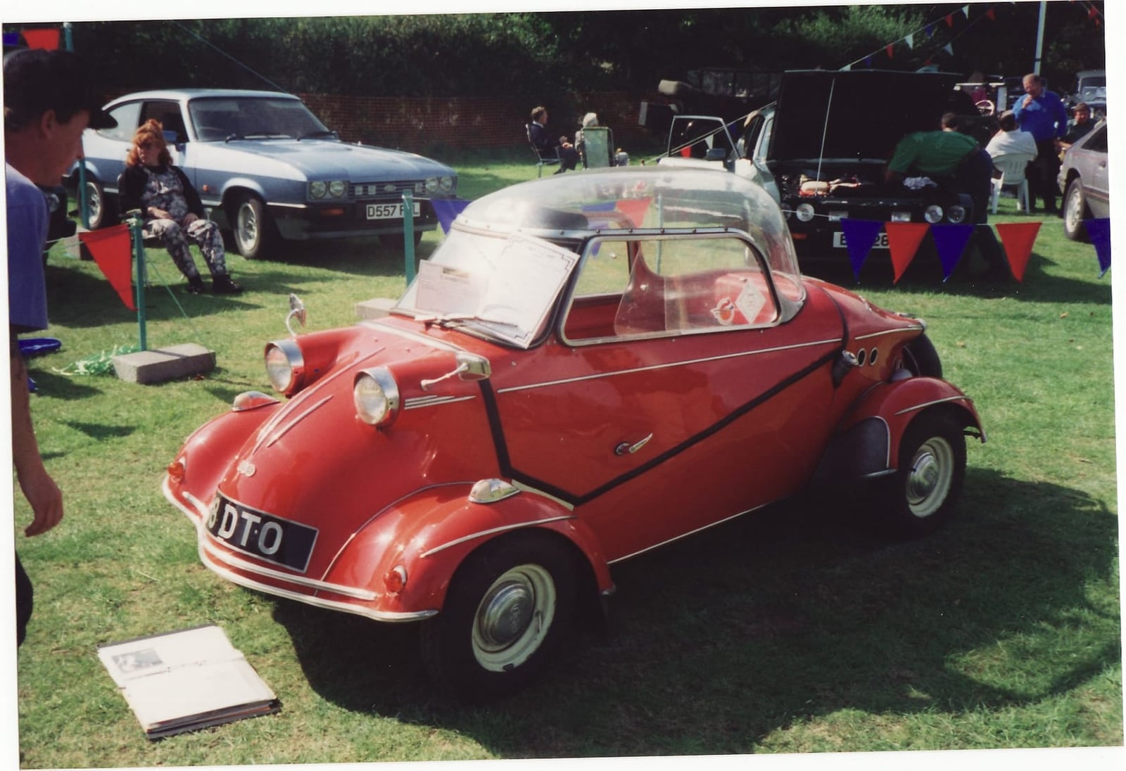 A red FMR TG500 Messerschmitt Tiger four-wheeler on grass at a classic vehicle show, front three-quarter view, private registration DTO