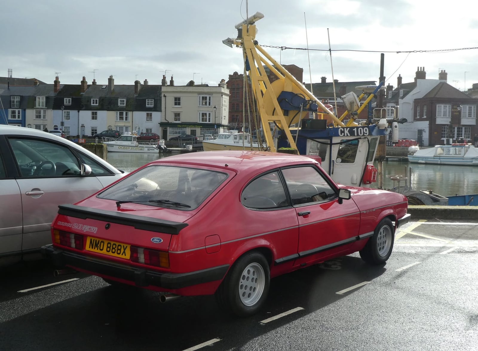 A red 1982 Ford Capri 2.8 Injection with a UK registration parked beside a harbour, rear three-quarter view