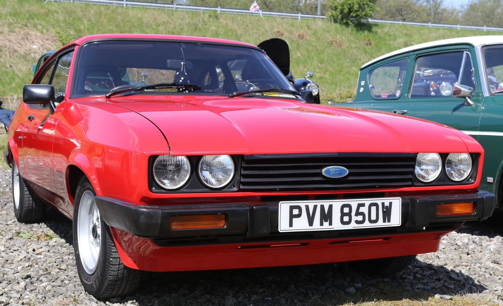 A red Ford Capri Mk3 with a UK registration parked on gravel at a show