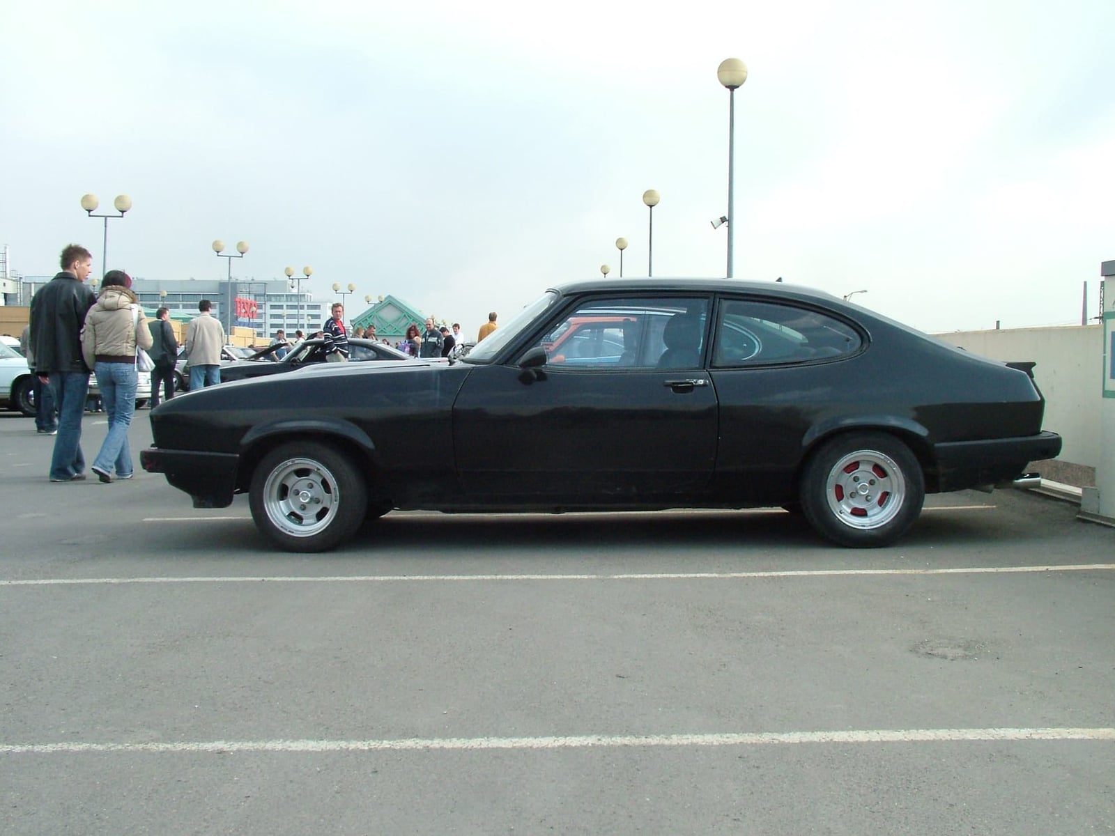 A black Ford Capri Mk3 parked in a car park at a classic car meeting, side view