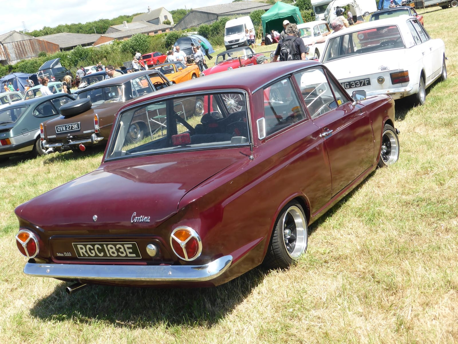 The rear three-quarter view of a maroon Ford Cortina Mk1 1500 De Luxe showing the circular tail lamps