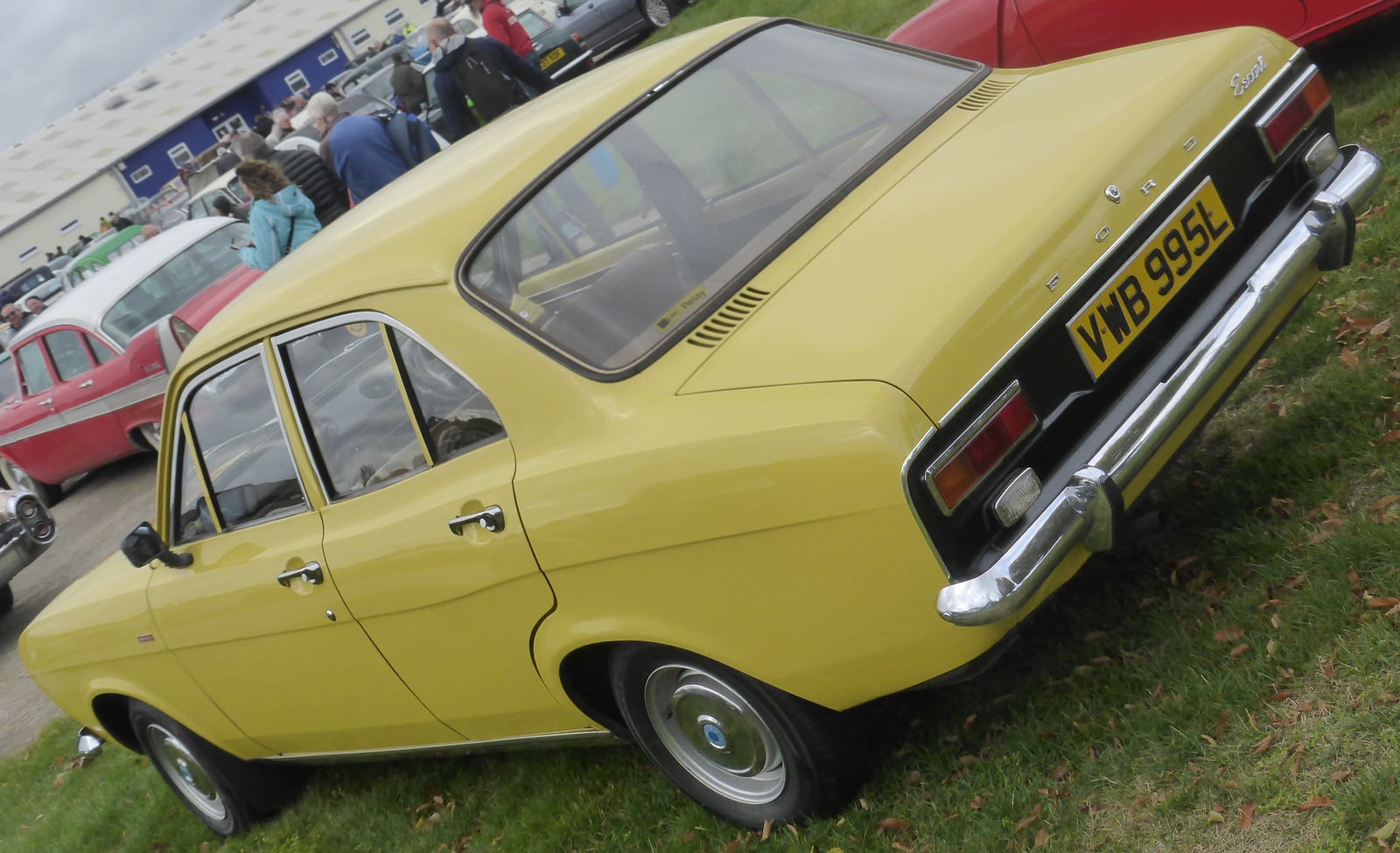 A yellow Ford Escort Mk1 1300XL four-door saloon at a show, rear three-quarter view