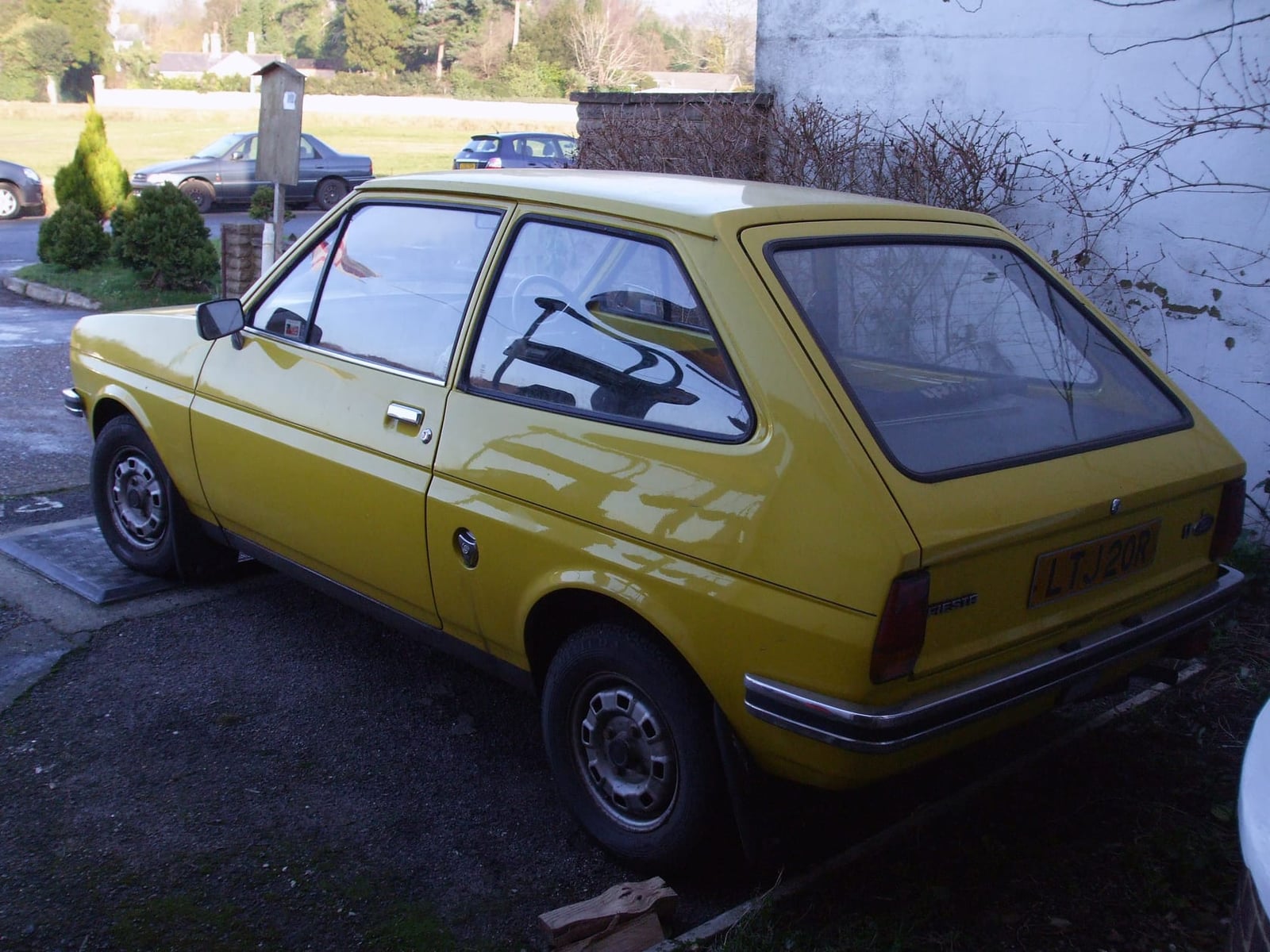 A gold Ford Fiesta Mk1 parked beside a wall, rear three-quarter view