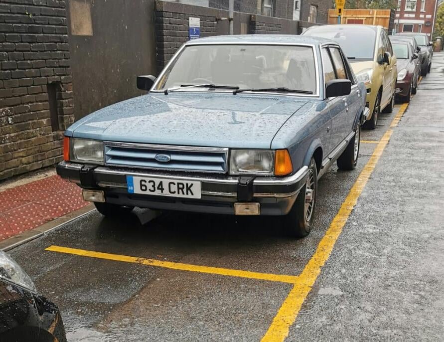 A light blue Ford Granada Mk2 Ghia X four-door saloon on a street, front three-quarter view