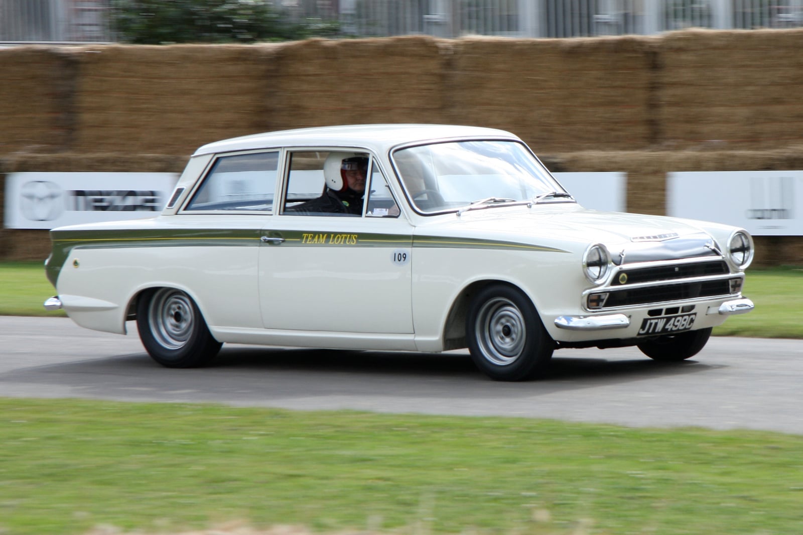 A white Ford Lotus Cortina Mk1 with a green side flash cornering at a circuit