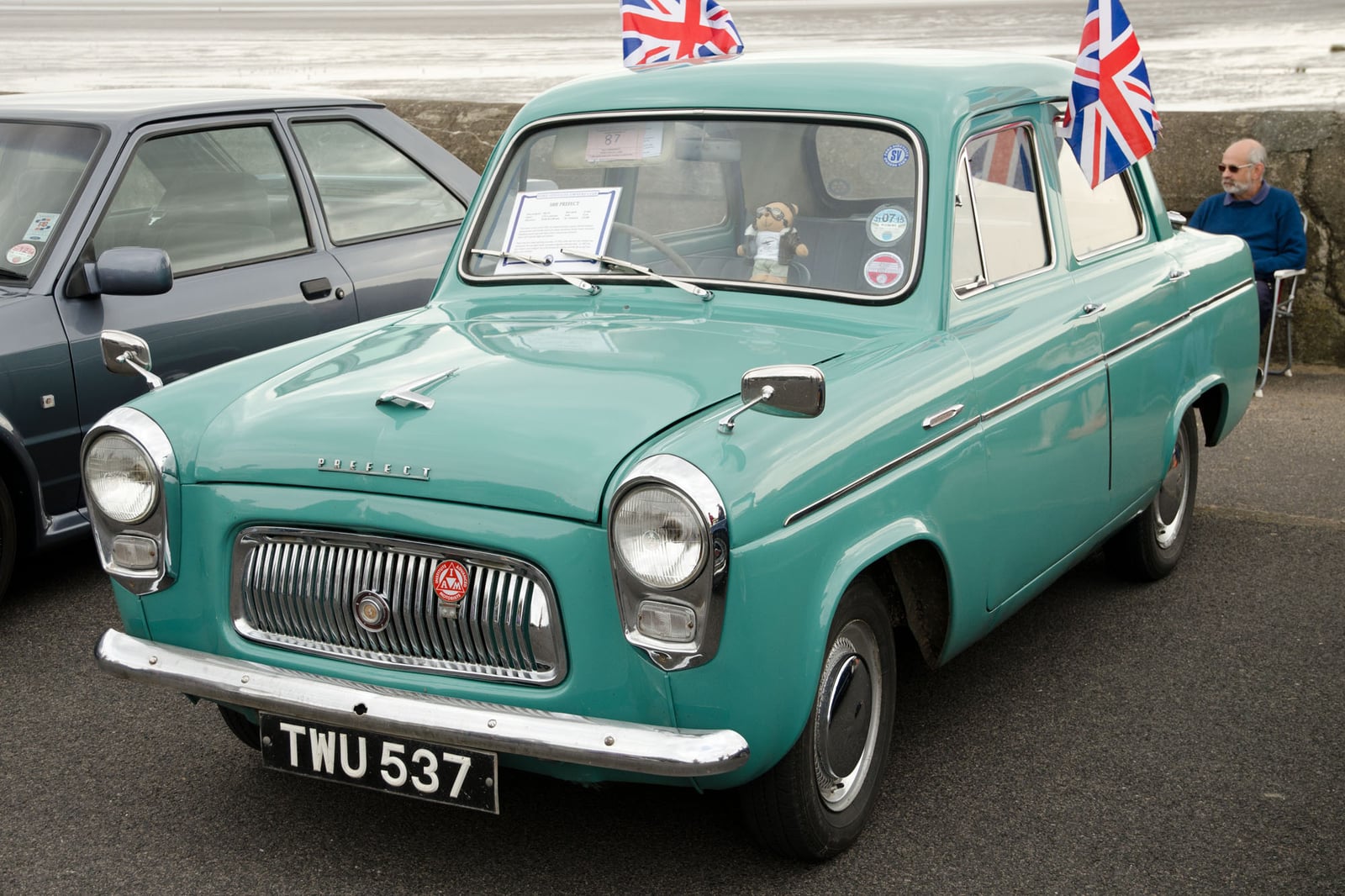 A turquoise Ford Prefect 100E saloon at a seaside show with Union Jack flags, front three-quarter view