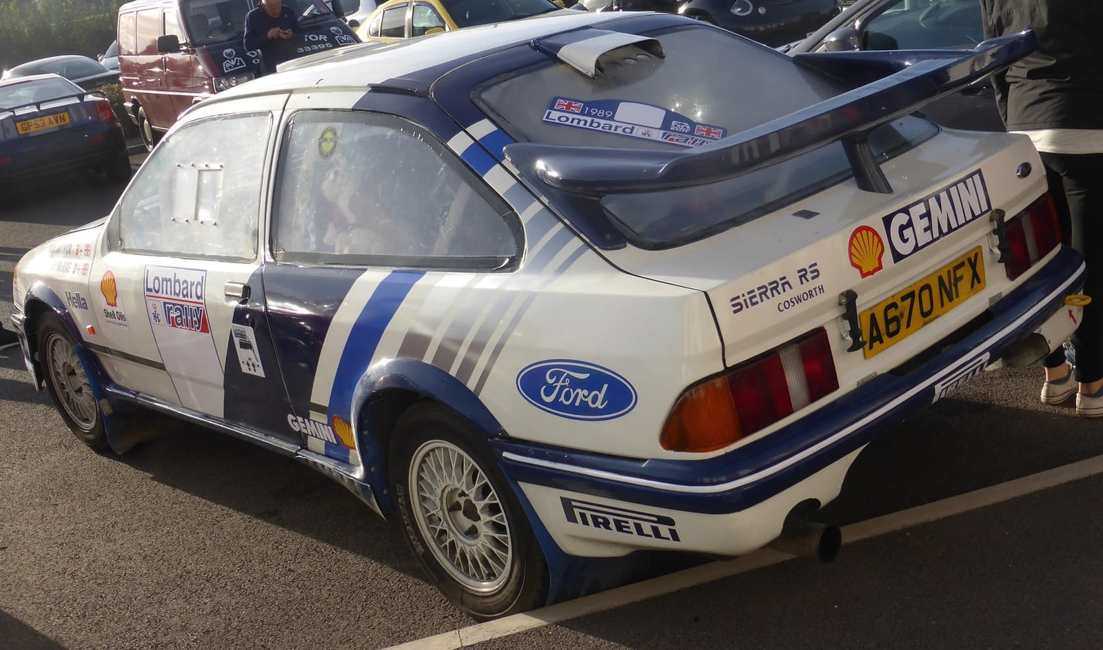 A white Ford Sierra RS Cosworth rally replica in blue Gemini and Shell livery, rear three-quarter view, UK registration A670 NFX