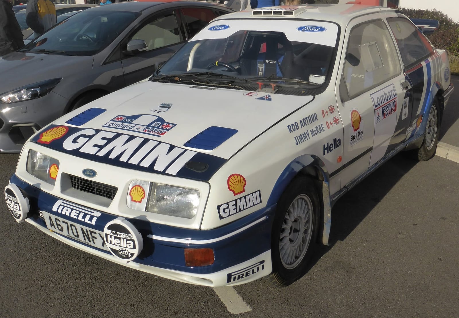 A white and blue Ford Sierra RS Cosworth in period Lombard RAC Rally livery with a UK registration at a show