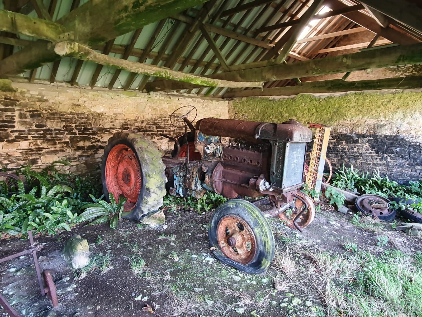 A rusty, derelict Fordson Major tractor standing in a tumbledown stone barn, overgrown and missing parts