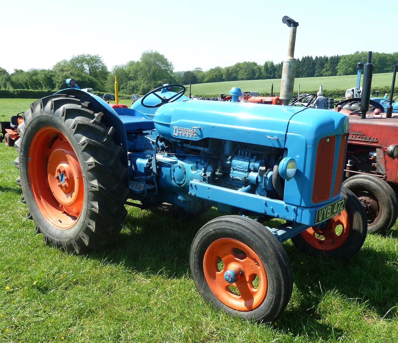 A blue Fordson New Major seen from the side on sunlit grass at a vintage rally