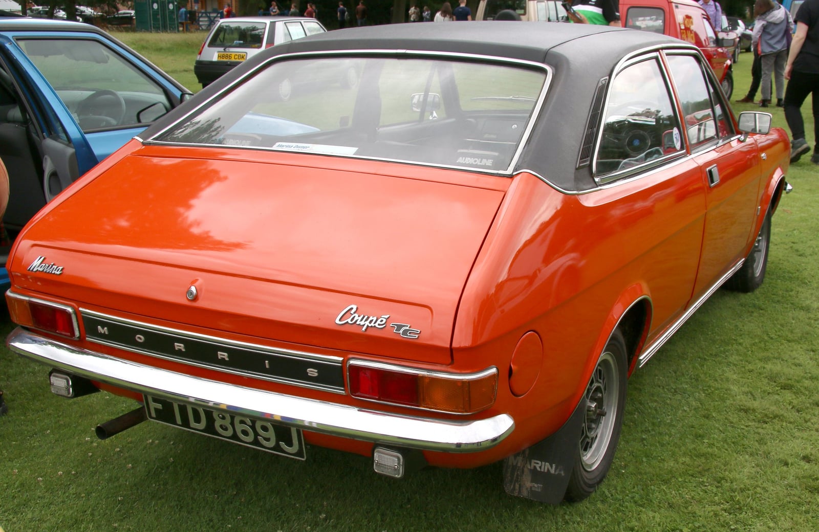 A red Morris Marina 1.8 TC Coupé with black vinyl roof (J plate, 1971), rear three-quarter view at an outdoor classic car show