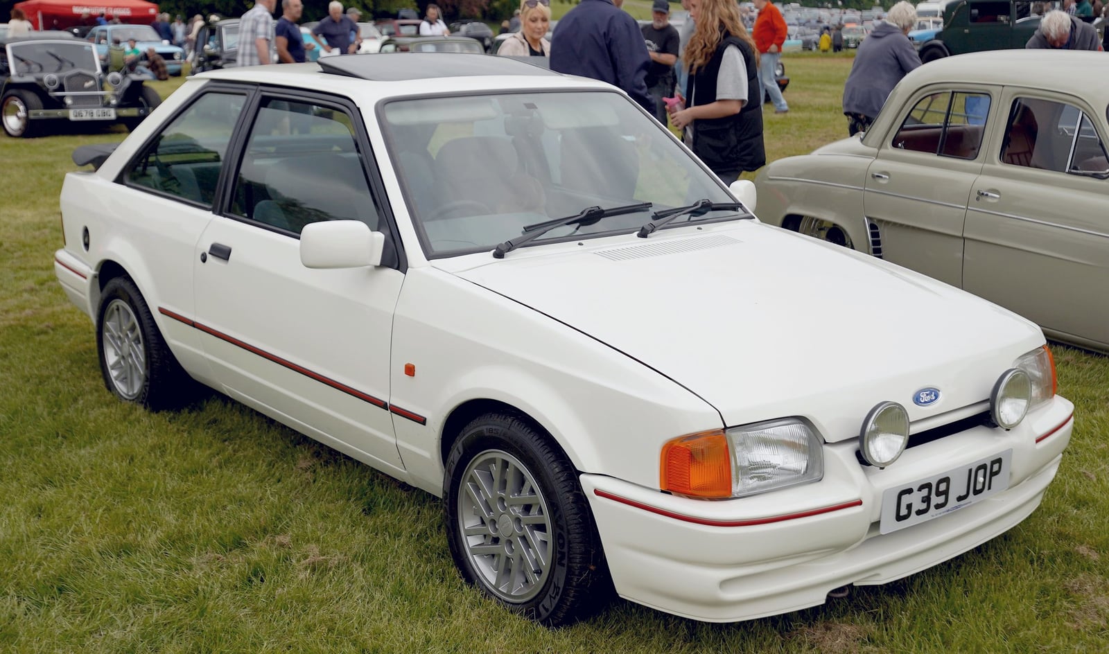 A white front-wheel-drive Ford Escort XR3i hatchback at a show, front three-quarter view
