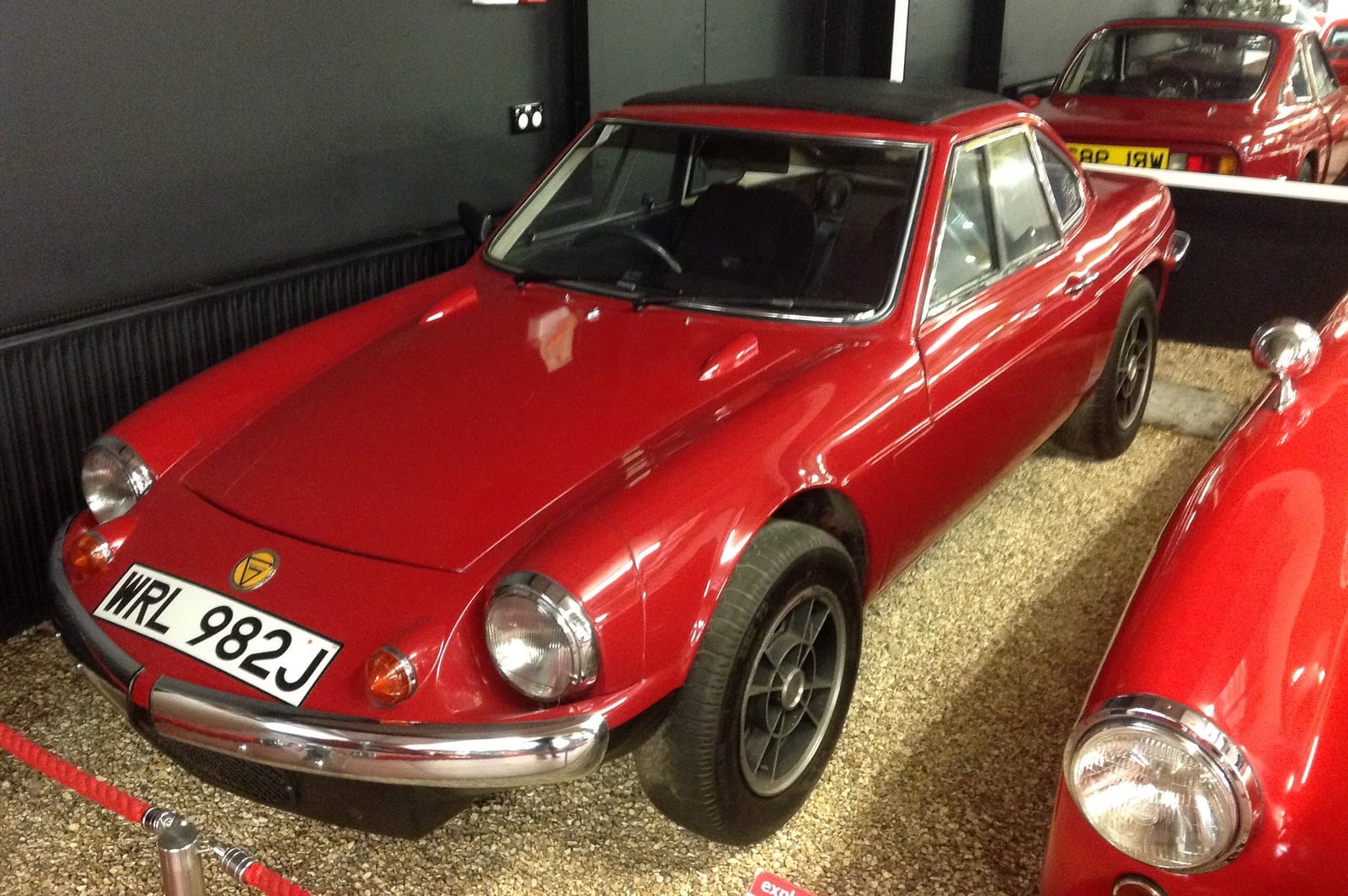 A red Ginetta G15 fitted with the 998cc Imp engine, registration MNE 982J, front three-quarter view indoors