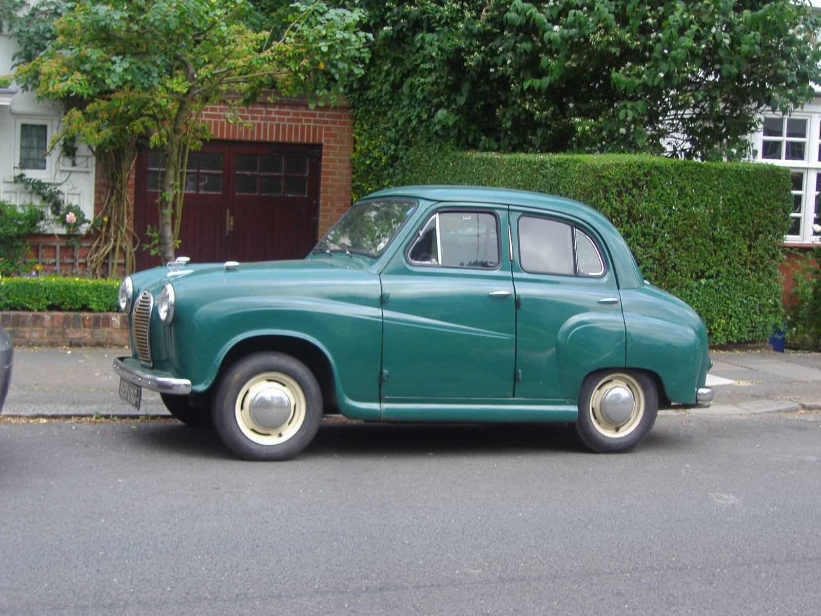 A green Austin A30 in side profile parked by a hedge