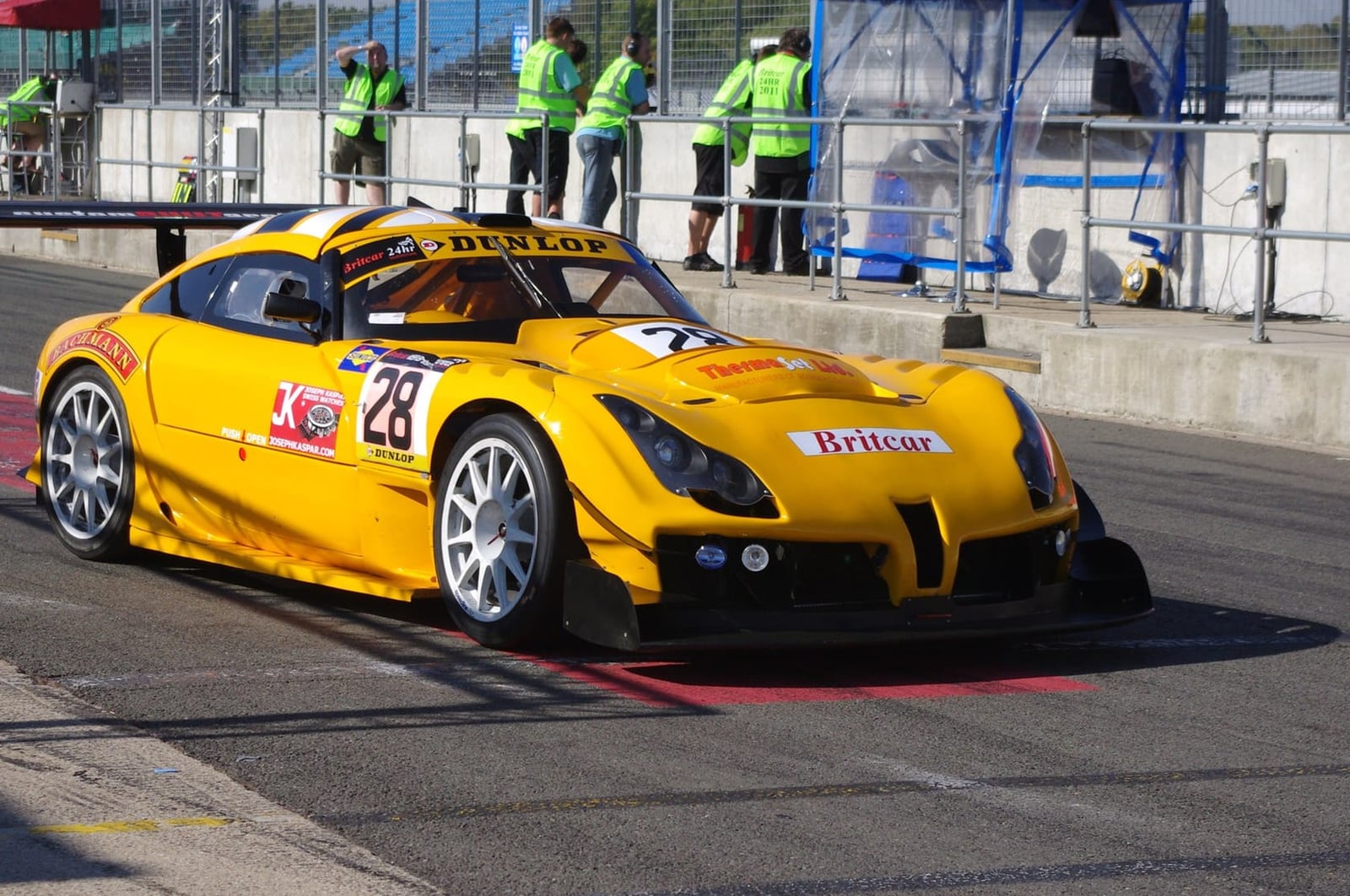 A yellow TVR Sagaris racing car with a number 28 on its door in a pit lane at a British circuit
