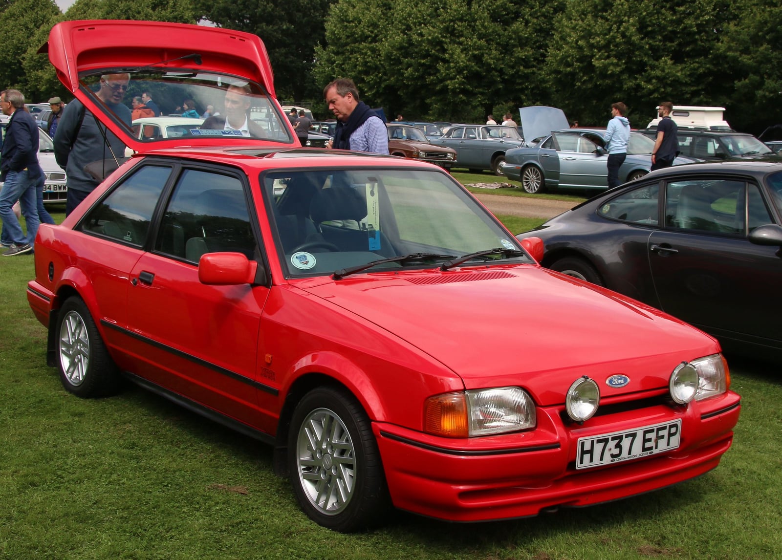A red Ford Escort XR3i hatchback with the tailgate open at a show