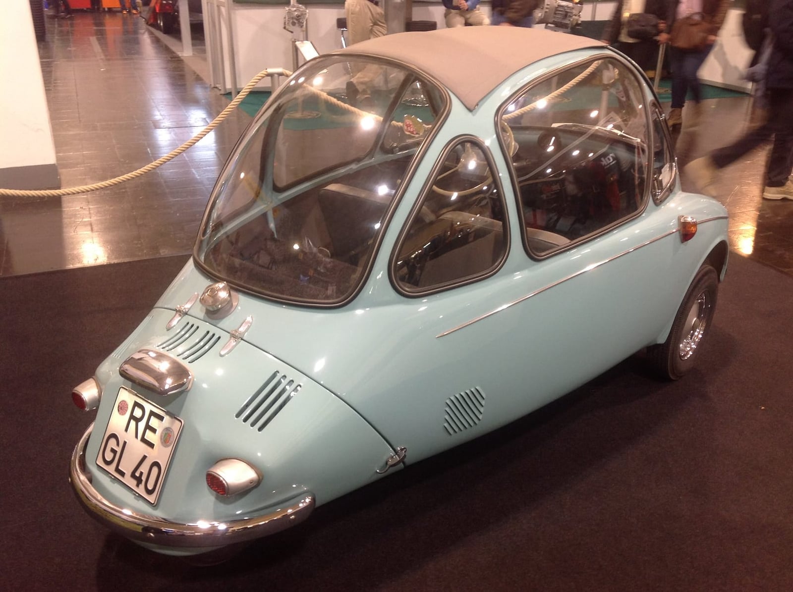 A pale blue Heinkel Kabine bubble car photographed head-on indoors, showing the single front-opening door and wraparound glass