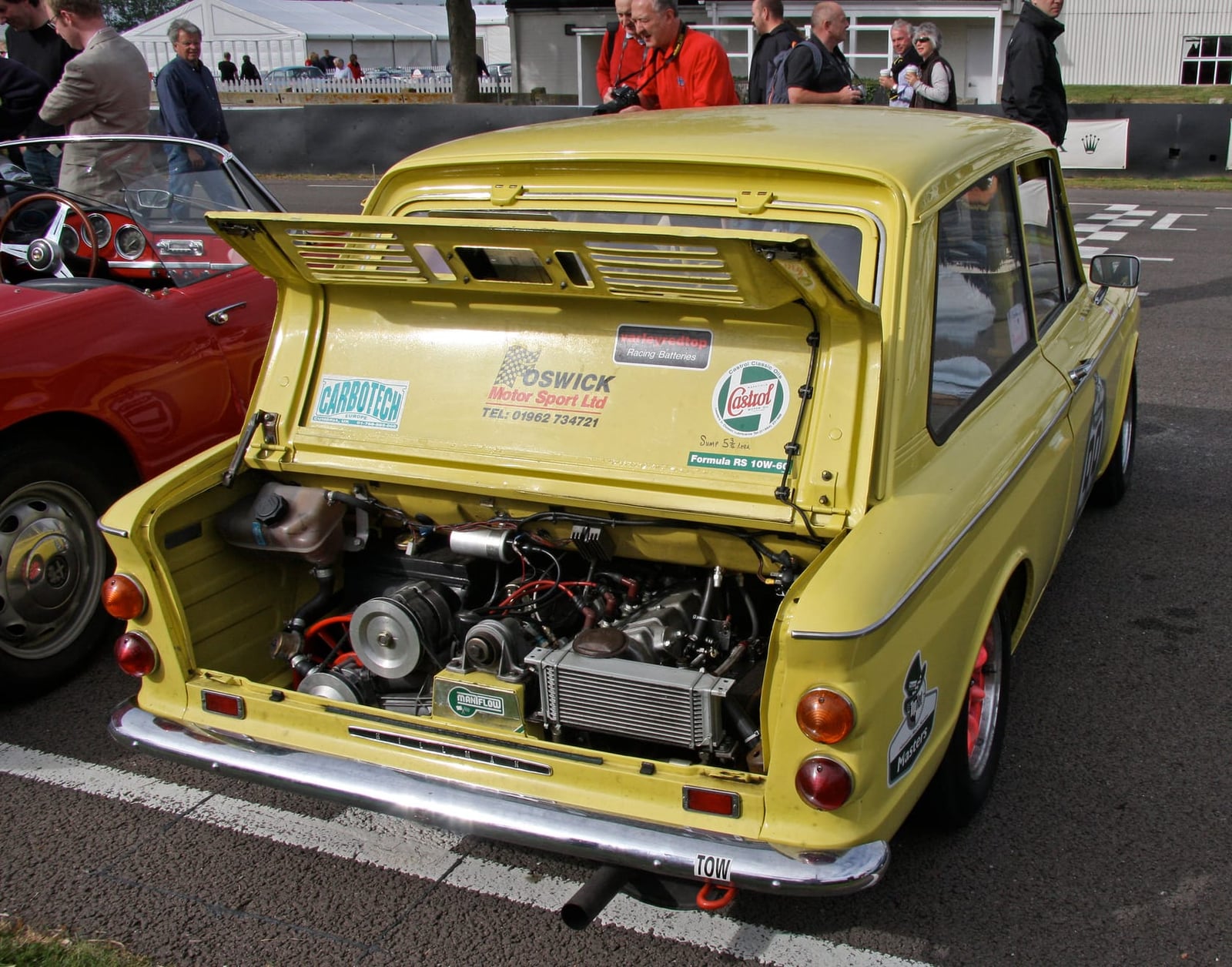 A yellow Hillman Imp with its rear engine cover raised, showing the aluminium engine mounted behind the axle