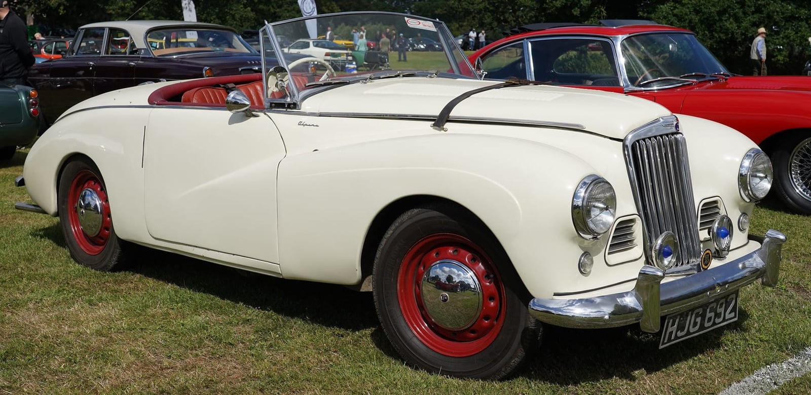 A cream 1954 Sunbeam Alpine with red wheels, side view, UK registration HJG 692