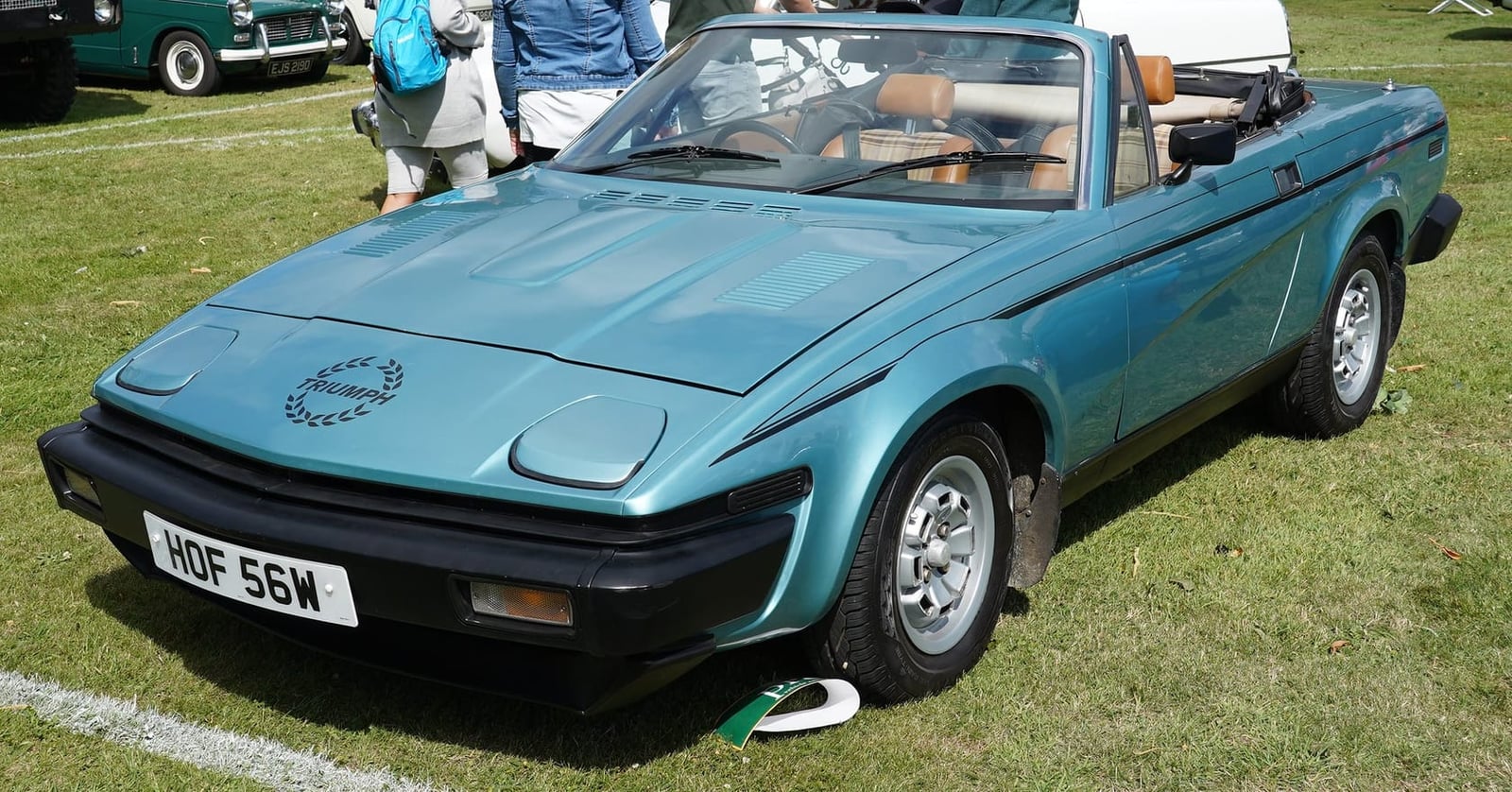 A metallic blue Triumph TR7 convertible with its roof down and a UK registration at an outdoor show